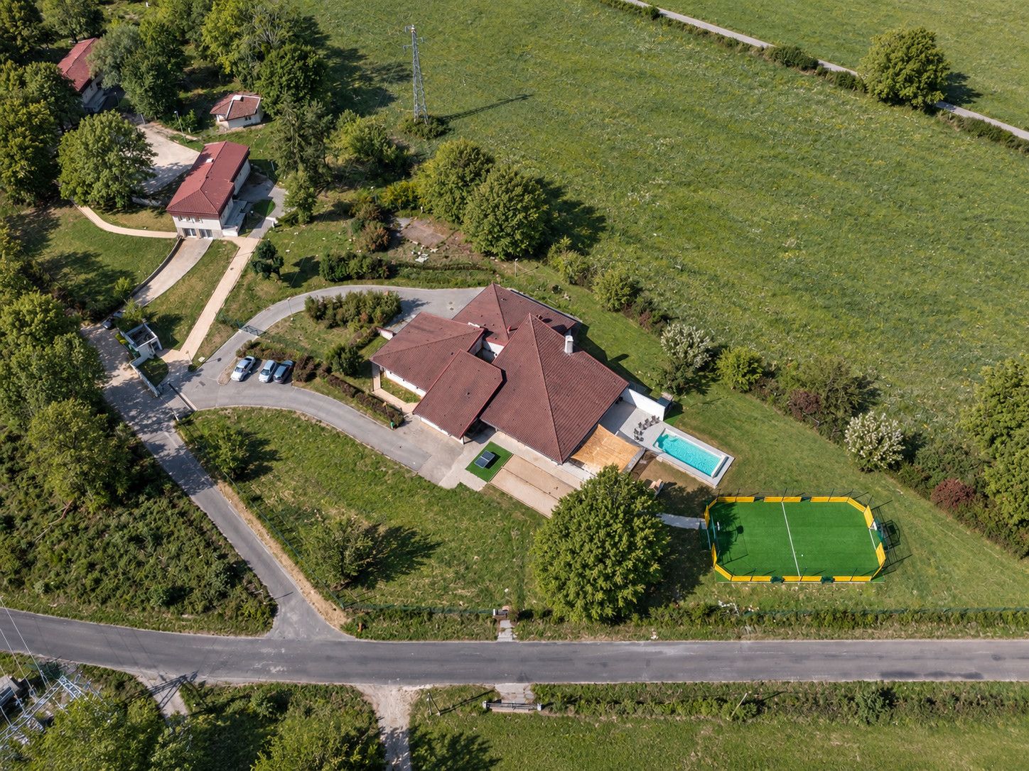 An aerial view of a residential area with a large house, a swimming pool, and a green sports field.