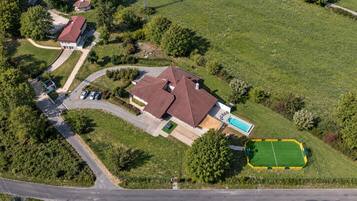 An aerial view of a residential area with a large house, a swimming pool, and a green sports field.