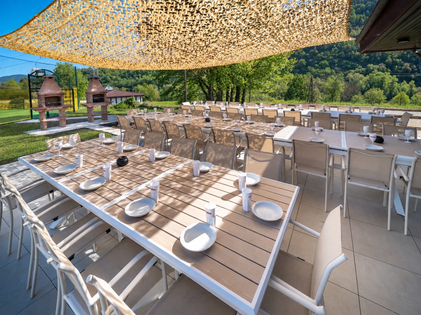 Un espace extérieur aménagé pour les repas, avec des tables et des chaises, une pergola au-dessus et une vue sur le paysage environnant.