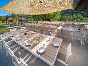 Un área de comedor al aire libre con mesas y sillas, una pérgola en lo alto y vistas del paisaje circundante.