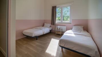 A bedroom with two single beds, a nightstand, a window with curtains, and a wooden floor.