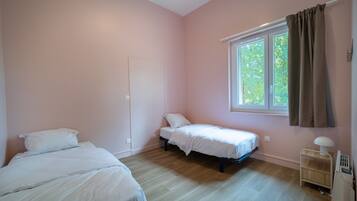 A bedroom with two beds, a window with curtains, and a bedside table with a lamp.