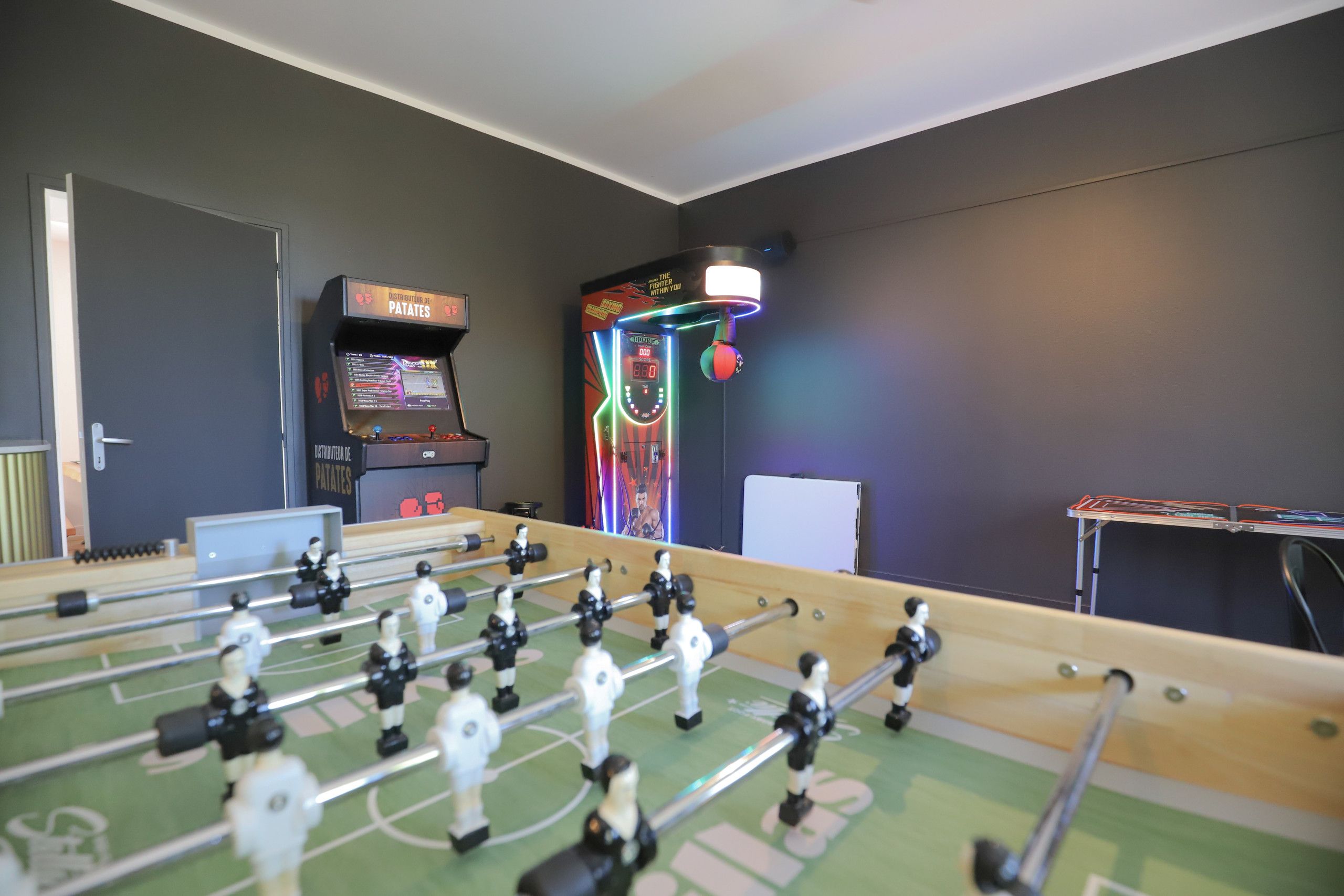Una habitación con mesa de fútbol de mesa, máquina de videojuegos y aro de baloncesto.