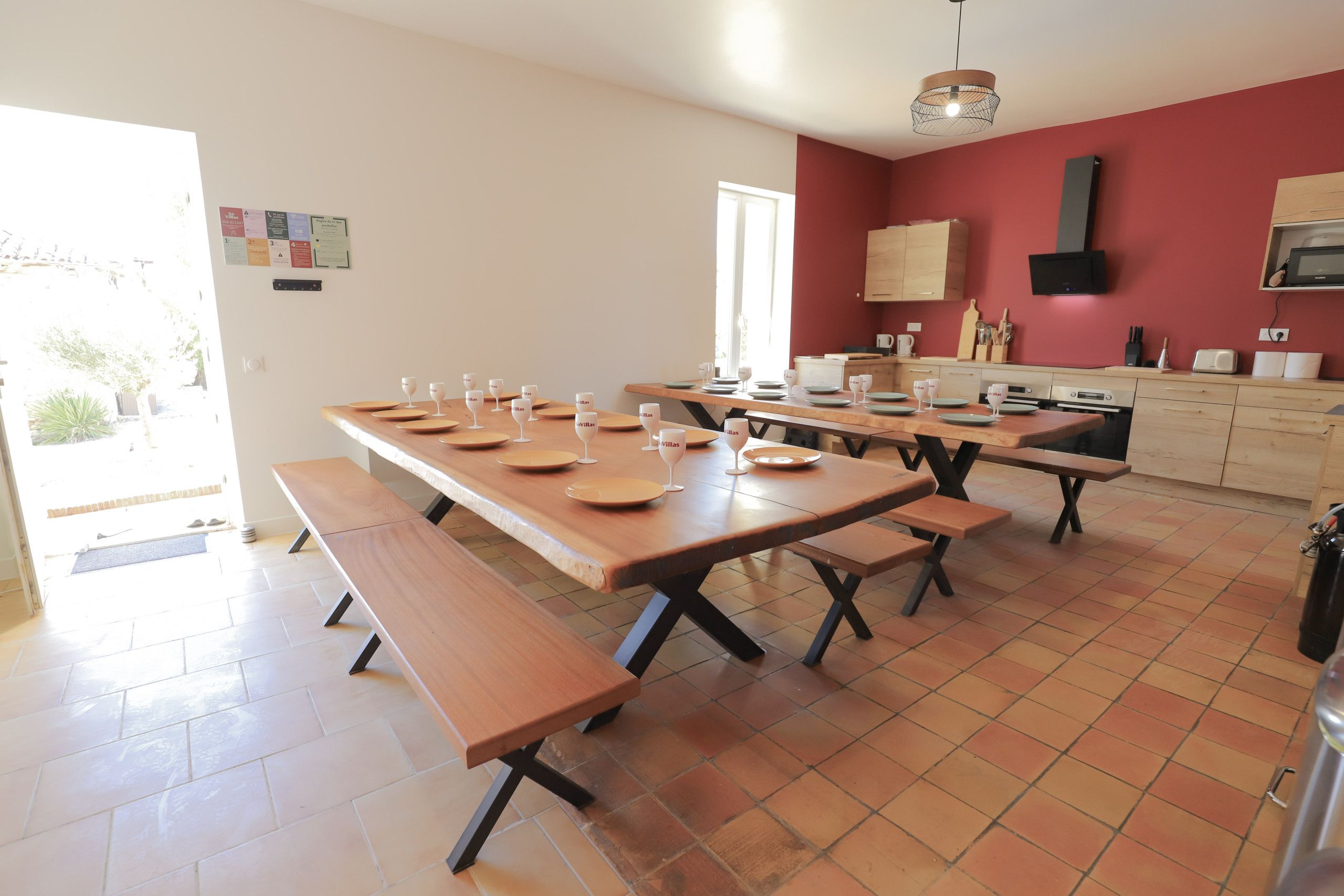 Een eetruimte met meerdere houten tafels en banken, een keuken met kasten en apparatuur, en uitzicht op het omliggende landschap.