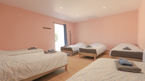 Habitació amb quatre llits disposats en forma de U, una finestra amb cortina i una porta amb penjador de tovalloles.