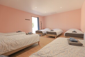 Quarto com quatro camas dispostas em formato de U, janela com cortina e porta com porta-toalhas.