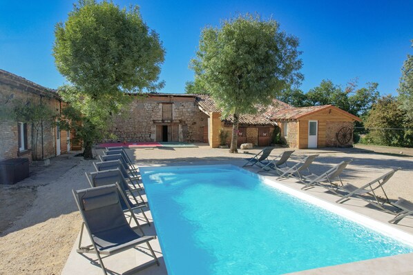 A swimming pool with lounge chairs, a stone building, and trees.