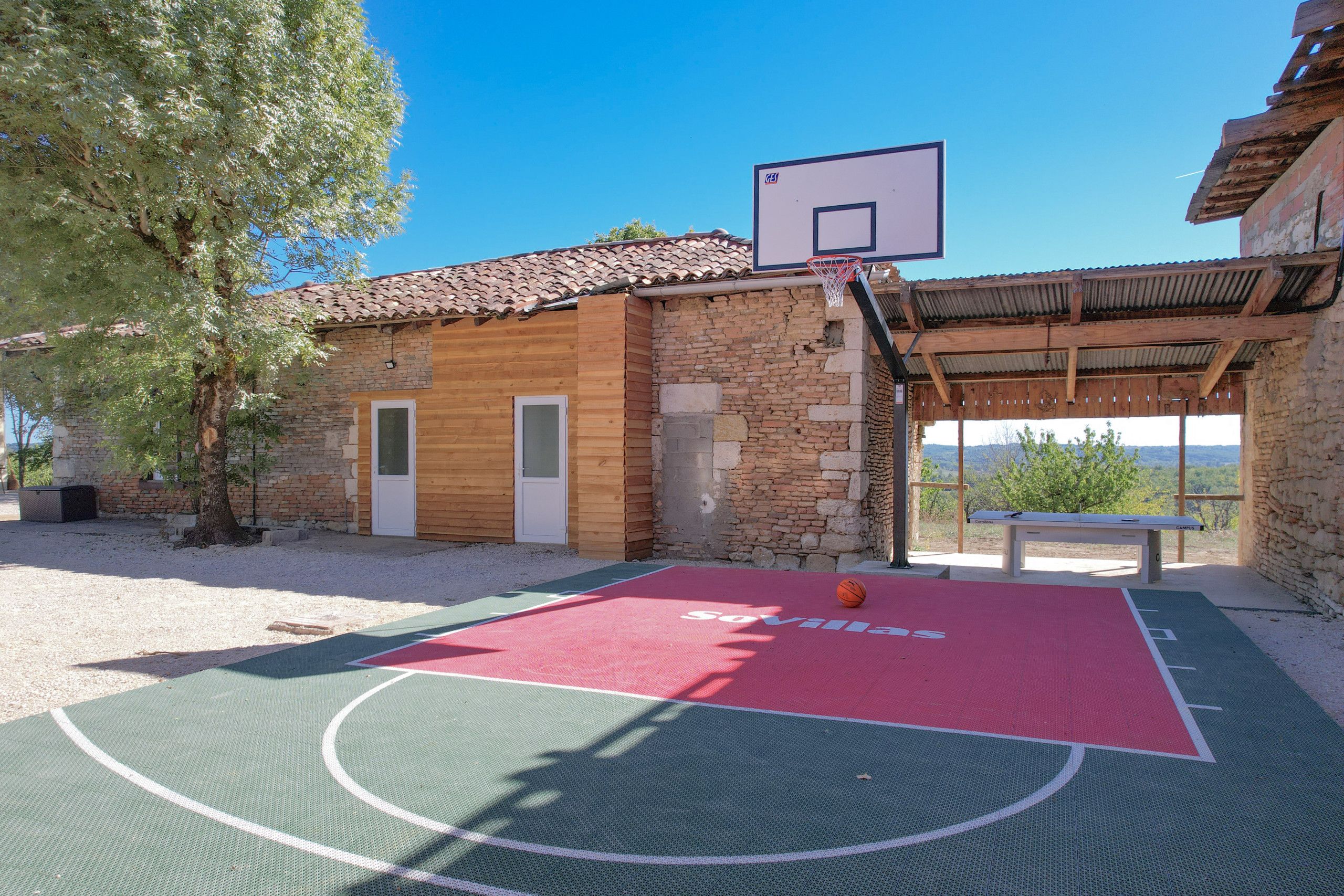 An outdoor basketball court with a red and green surface, a basketball hoop, and a bench.