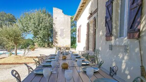 Zona d'esmorzar a l'aire lliure amb una taula de fusta llarga preparada per a dinar, envoltada de cadires.