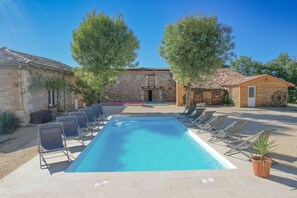 A swimming pool with lounge chairs, a stone building, and a wooden structure.