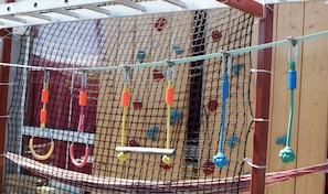 Un espace de jeux sécurisé par un filet, équipé de divers éléments d’escalade et de jeux suspendus.
