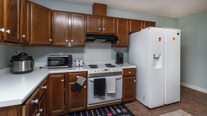Una cocina compacta con armarios de madera, microondas, tostadora, estufa, horno y refrigerador blanco.