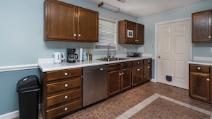 A kitchen with wooden cabinets, a dishwasher, a coffee maker, and a trash can.