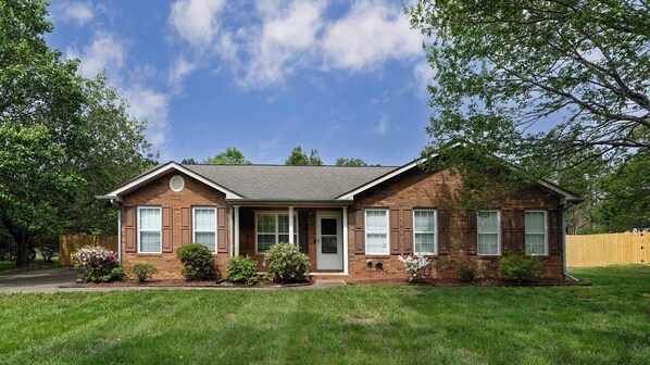 A single-story brick house with a front porch, a garage, and a well-maintained lawn.