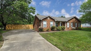 A two-story brick house with a front porch, a driveway, and a wooden fence.