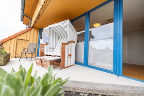 A patio with a white striped chair, a wooden bench, and a small table. - Dancing lighthouse (Wittdün)