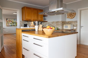 A modern kitchen with wooden cabinets, a central island with drawers, a microwave, and a fruit bowl. - Dancing lighthouse (Wittdün)