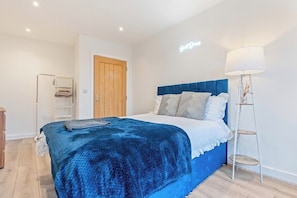 A bedroom with a bed, a bedside lamp, a wooden door, and a shelf.