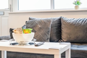A living room with a sofa, a white coffee table, and a bowl of snacks.