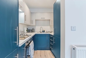 A compact kitchen with white cabinets, a blue accent wall, a sink, and a stove.