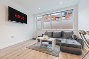 A modern living room with a grey sofa, a white coffee table, and a flat-screen TV mounted on the wall. - Modern CityCentre|Netflix|Smart TV|Free Parking (Nottingham)