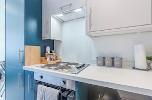 A compact kitchen with a gas stove, cabinets, and a countertop with storage containers.