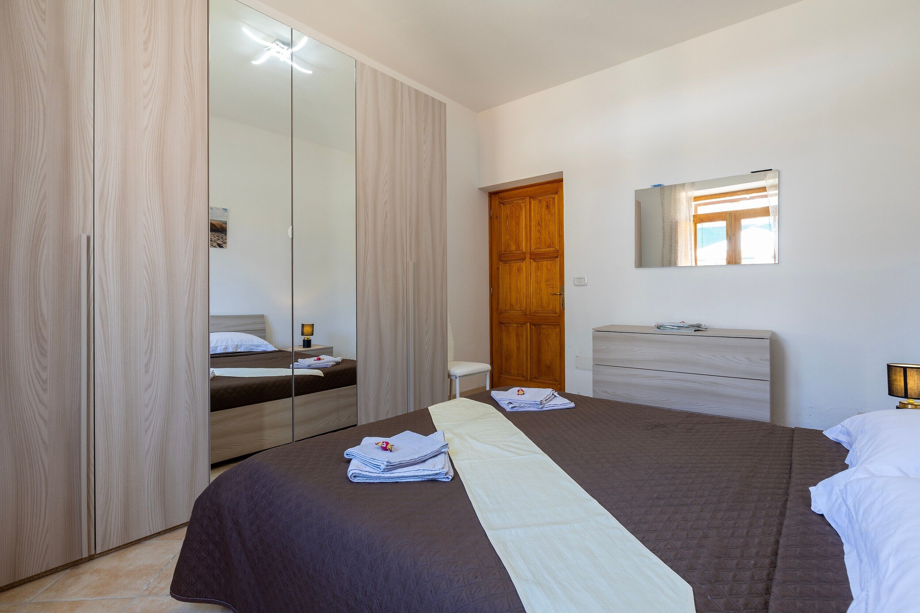Een slaapkamer met een bed, een kledingkast, een spiegel, een dressoir en een raam.