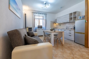 Une cuisine moderne avec des meubles blancs, une table à manger avec des chaises, un canapé avec des coussins et un téléviseur.