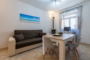Een moderne woonkamer met een bank, eettafel, stoelen, een televisie en een schilderij aan de muur.