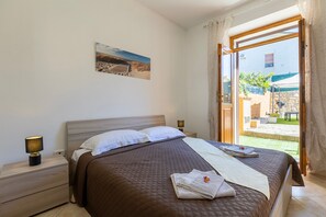 Een slaapkamer met een bed, nachtkastje, lamp, schilderij en uitzicht.