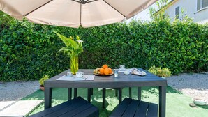 En udendørs terrasse med et bord dækket til morgenmad, inklusive frugt, en tepotte og kopper.
