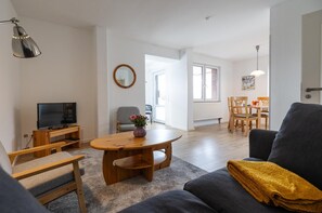 A living room with a TV, sofa, coffee table, and a dining area with chairs and a table.