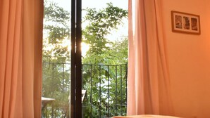 Et værelse med en seng, en balkon med gelænder og udsigt til træer og en bygning.