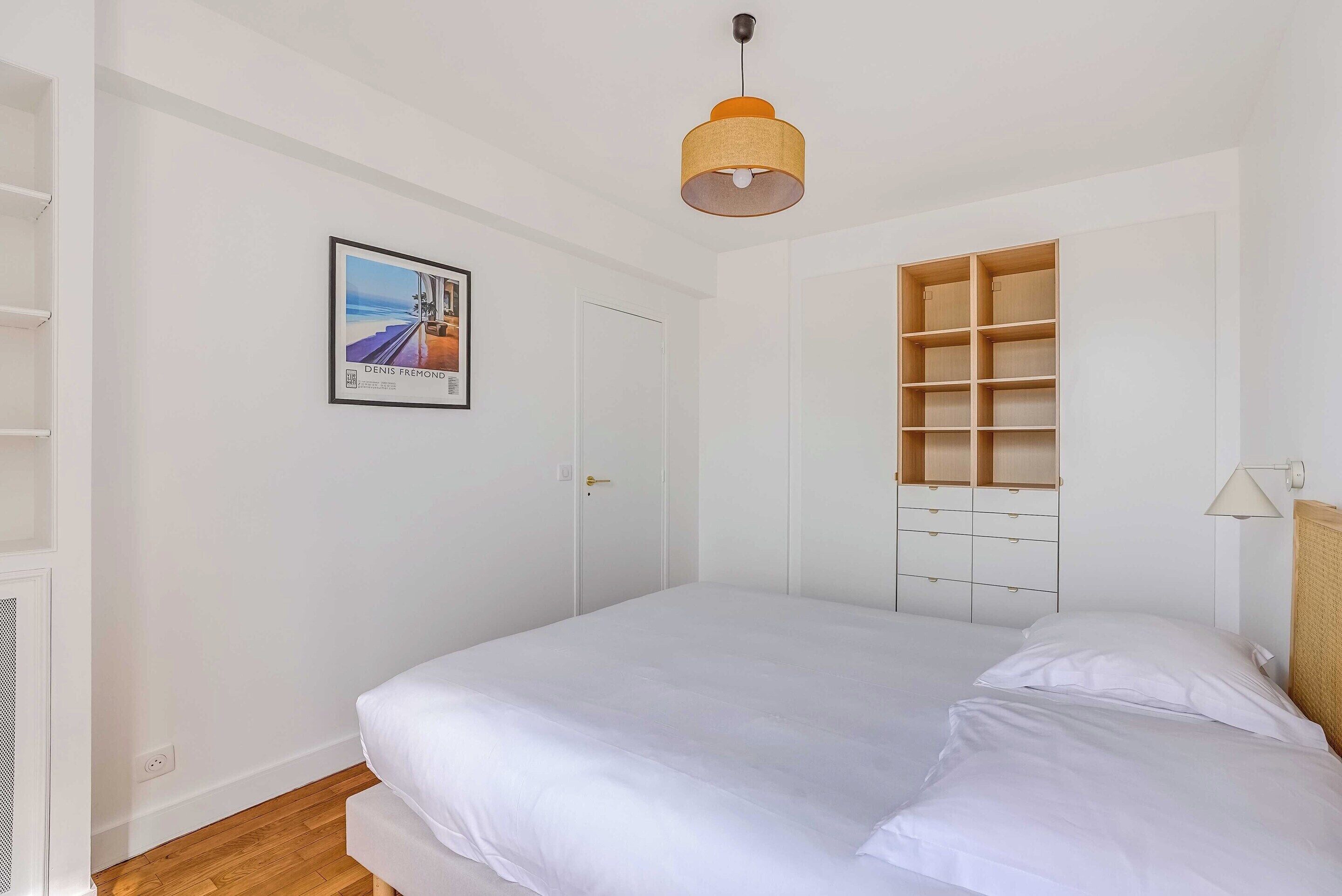 Een slaapkamer met een bed, een hanglamp, een deur en een ingebouwde boekenkast.