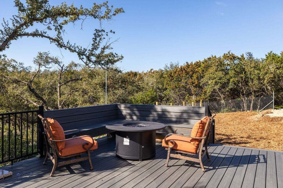An outdoor deck with a round table and two chairs, surrounded by a wooden deck and a metal fence.