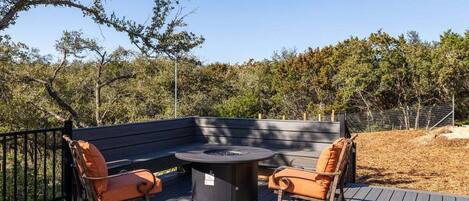 An outdoor deck with a round table and two chairs, surrounded by a wooden deck and a metal fence.