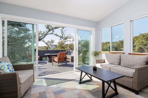 Una sala moderna con un sofá, una mesa de centro y una silla. Hay una puerta de vidrio que da a un patio al aire libre con una mesa y sillas.