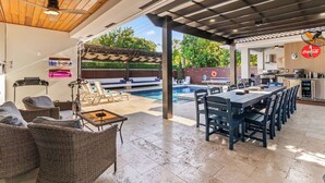 Un espace extérieur abrité comprenant une piscine, une table à manger, des chaises, des meubles en osier et un coin cuisine.