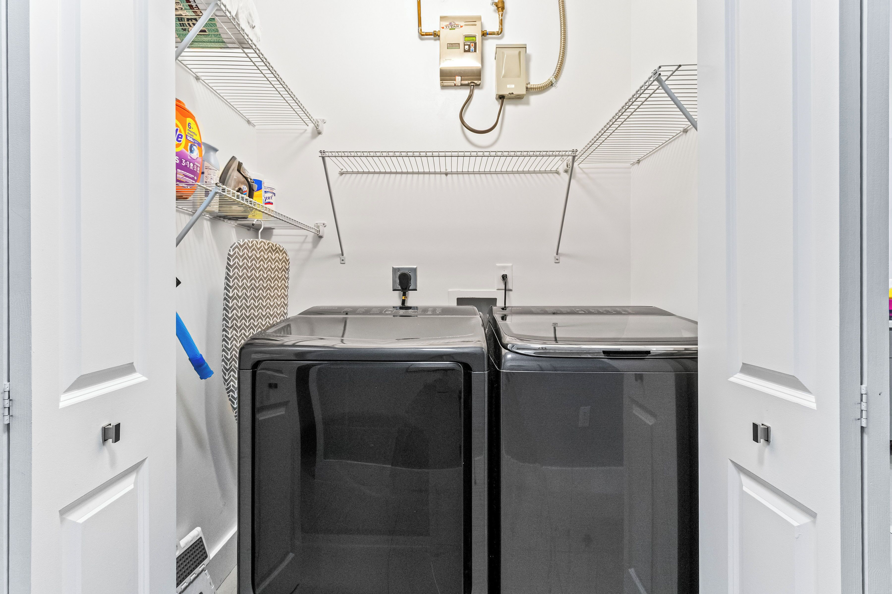 A compact laundry room with two large washing machines, a metal drying rack, and a small shelf with cleaning supplies.