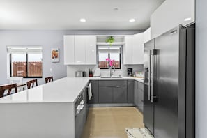 A modern kitchen with a large island, stainless steel appliances, and a window with a view. - Villa Sunset by Glam Homes (Hialeah)