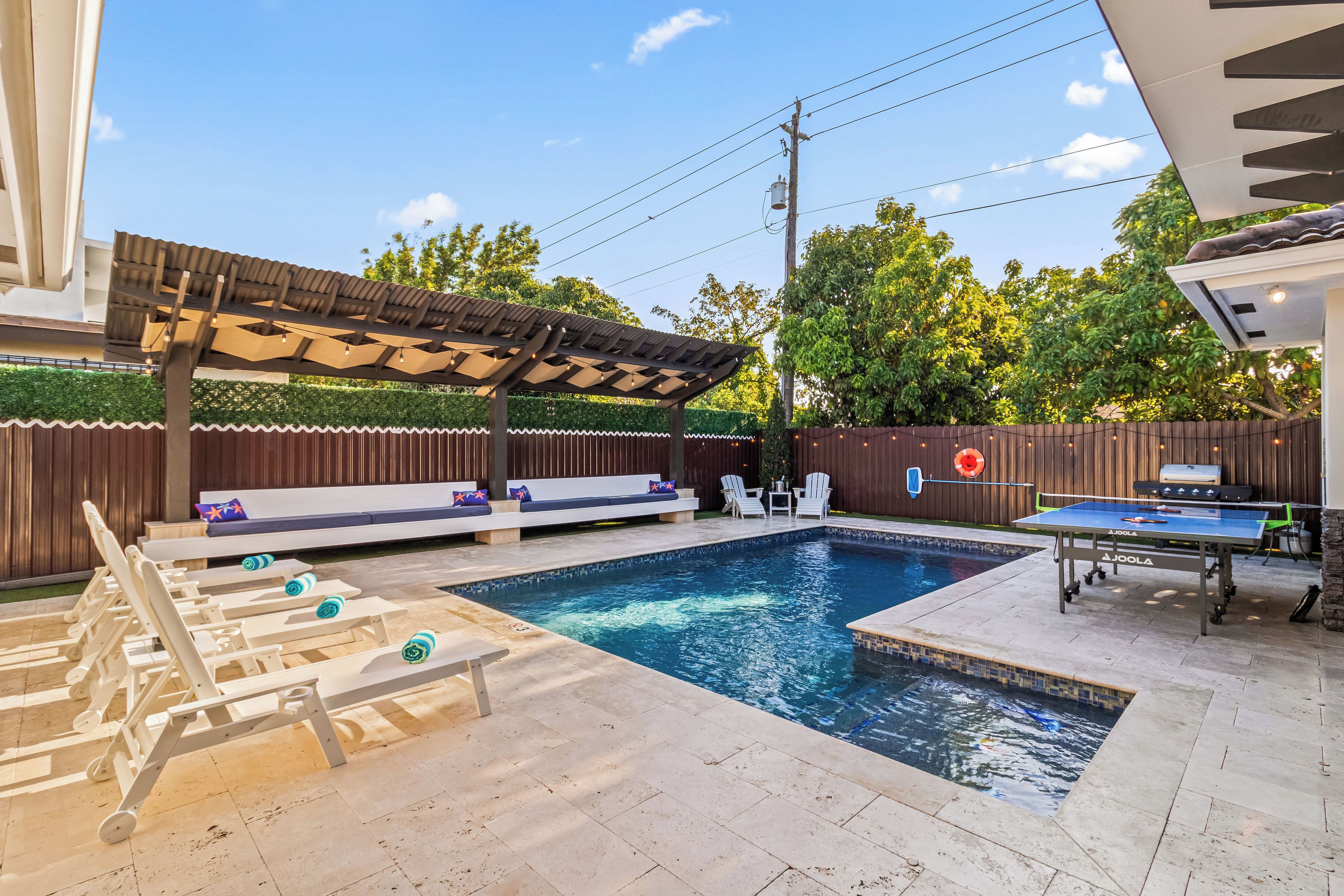A backyard with a swimming pool, outdoor seating, and a ping pong table.