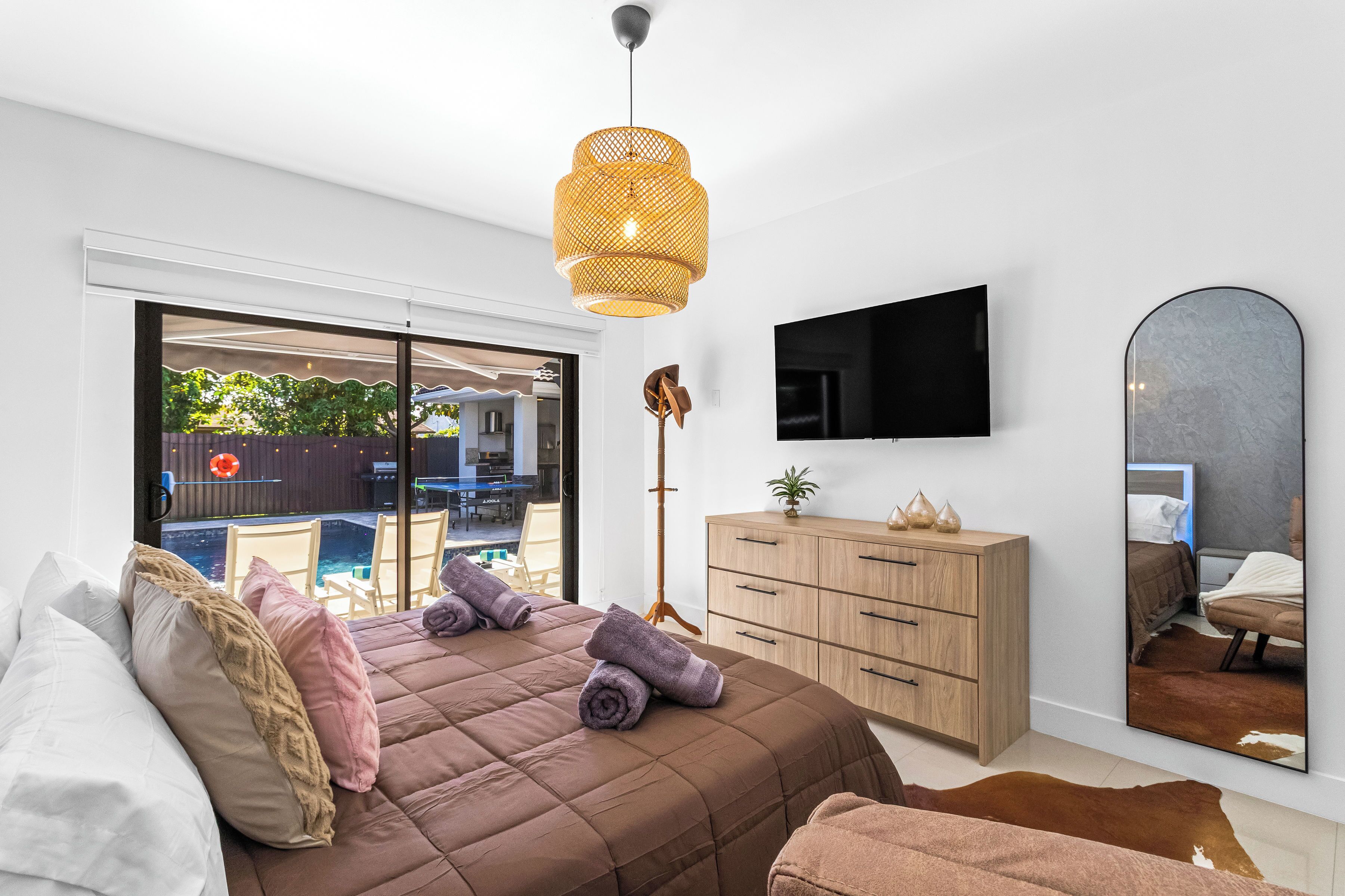 A bedroom with a bed, a wooden dresser, a television, and a large mirror.