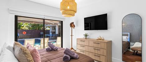A bedroom with a bed, a wooden dresser, a television, and a large mirror.