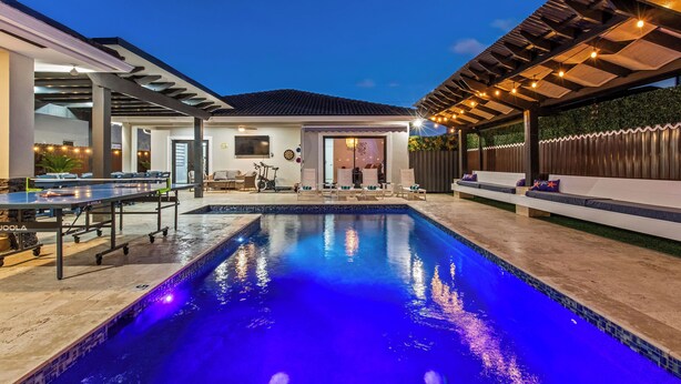 Une piscine agrémentée d’une pergola et d’un espace détente, une terrasse couverte et une vue sur la maison.