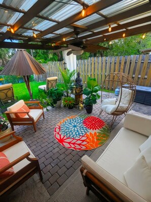 Een overdekt terras met zitplaatsen, een decoratief vloerkleed en een beeld.