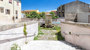 A narrow alleyway with a stone staircase leading to a small courtyard, surrounded by buildings with balconies and air conditioning units. - Charming Penthouse in Historic Village near the Sea (Nulvi)