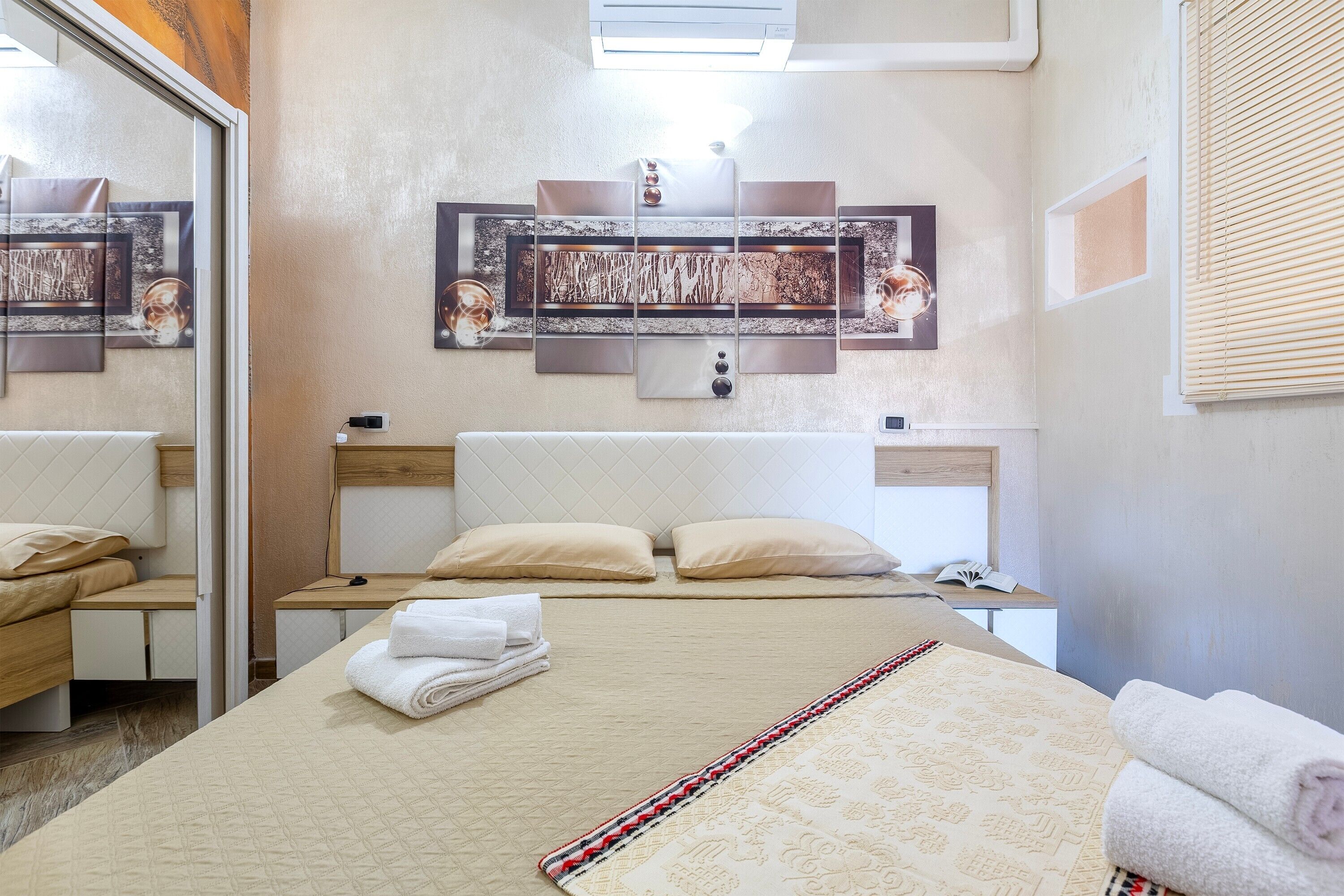Quarto de hotel com cama, mesas de cabeceira, espelho e obras de arte na parede.