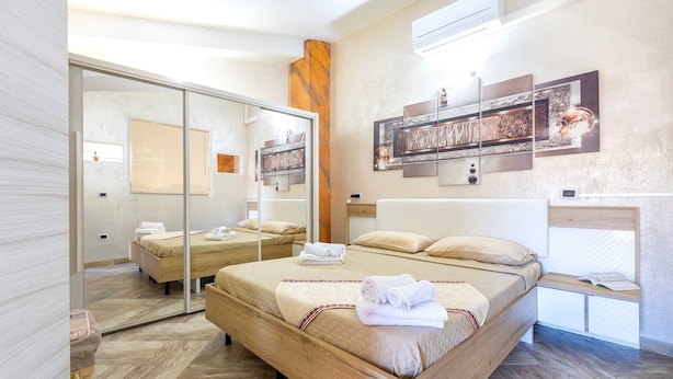 A modern hotel room with a large bed, a mirror, a wooden headboard, and artwork on the wall. - Charming Penthouse in Historic Village near the Sea (Nulvi)