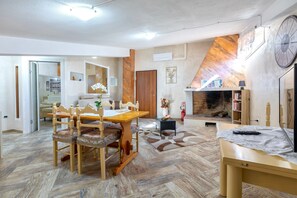 Een eethoek met een houten tafel en stoelen, een open haard en een televisie op een bijzettafeltje.