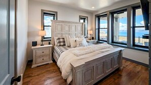 Ein Schlafzimmer mit einem großen Bett, zwei Nachttischen, einer Kopfteil und Blick durch große Fenster.